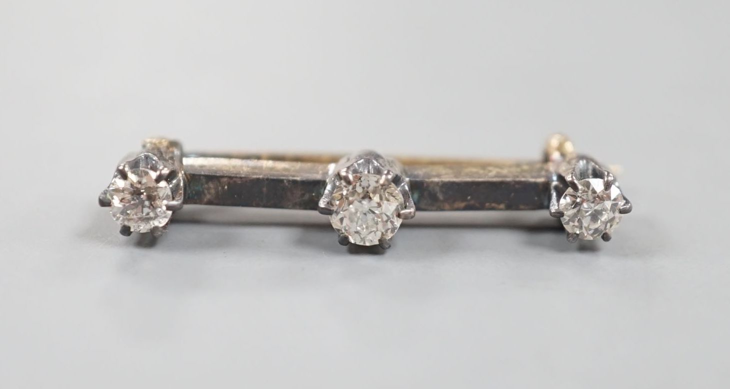 An early 20th century yellow metal and three stone diamond set bar brooch, 26mm, gross 2.1 grams.